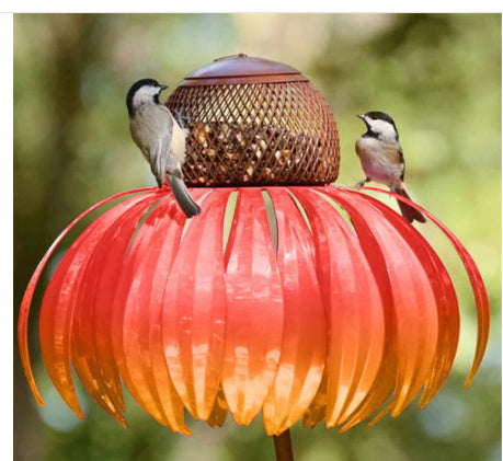 Two birds perched on a red and orange bird feeder with a blurred green background