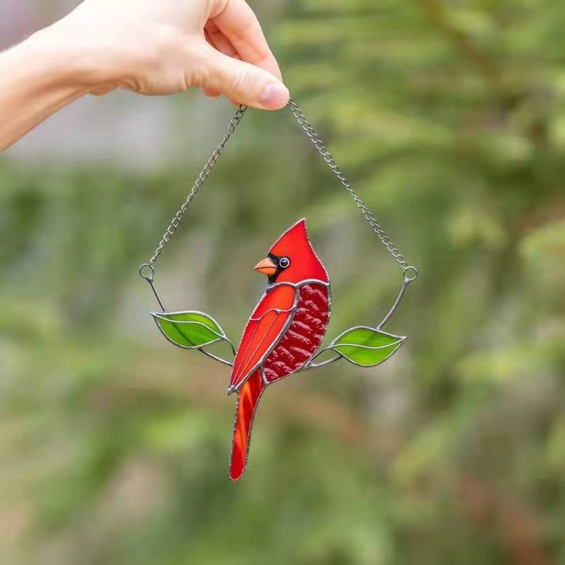 Stained glass red cardinal bird hanging ornament against a blurred green background