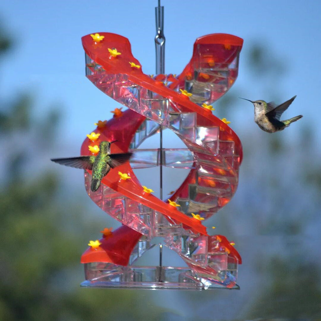 Hummingbird feeder with red spiral design and hummingbirds around it against a blue sky background.
