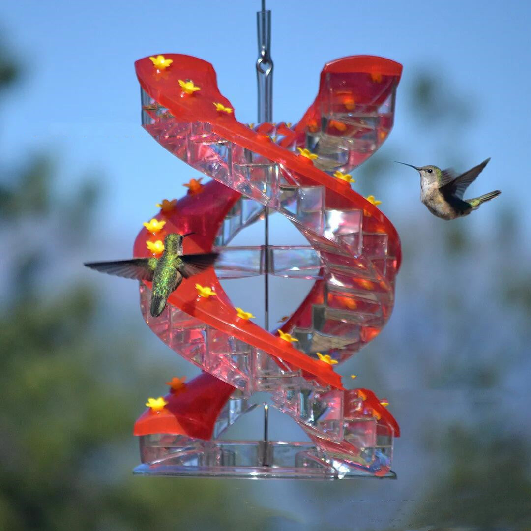 Hummingbird feeder with red spiral design and hummingbirds around it against a blue sky background.