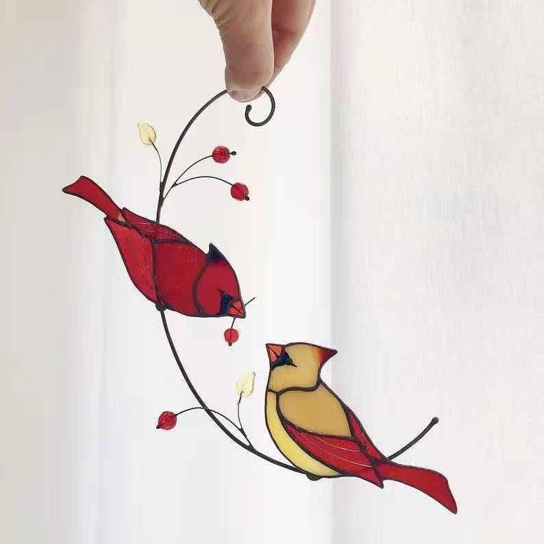 Stained glass window hanging with two cardinals on a branch.